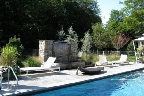 Elegant outdoor living space with inground pool, lounge chairs, and garden features in Long Island. Beautiful backyard with inground pool, outdoor furniture, and lush greenery.