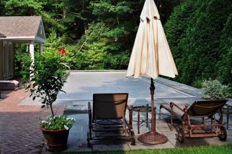 Relaxing outdoor pool area with lounge chairs, umbrella, and lush greenery in Long Island. Inground pool with outdoor furnishings and umbrella in Long Island.