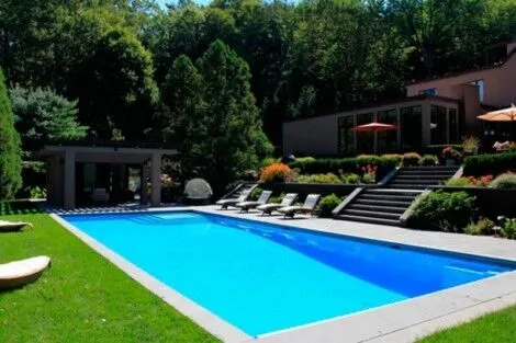 Beautiful inground pool with outdoor seating and lush greenery in Long Island backyard. Inground pool with modern outdoor furnishings and lush landscaping.