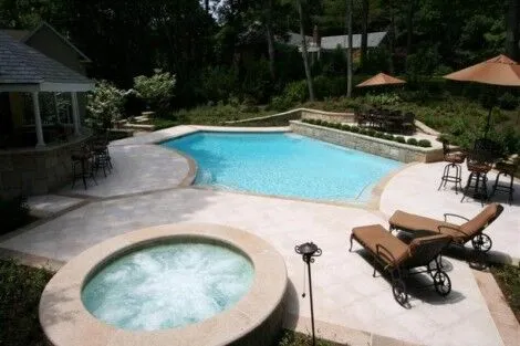 Beautiful geometric inground pool with hot tub, outdoor seating, and lush landscaping in Long Island backyard. Geometric inground pool with hot tub and outdoor furnishings in backyard.