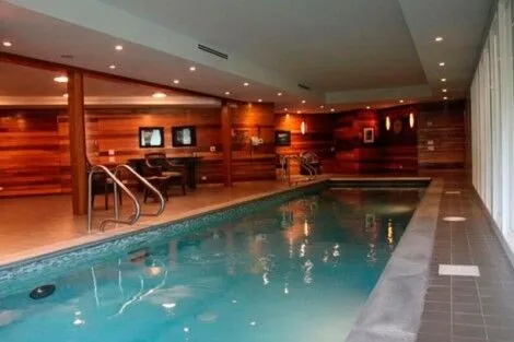 Elegant indoor pool with wooden accents and comfortable seating area, perfect for relaxation and recreation. Luxurious indoor pool with wooden walls and modern amenities.
