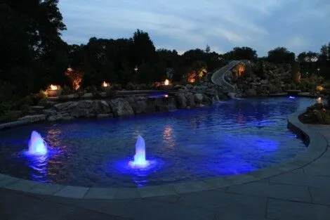 Elegant inground pool with waterfalls and lighting, perfect for outdoor relaxation and entertainment. Beautiful illuminated inground pool with waterfalls and fountains at dusk.
