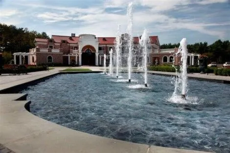 Luxury estate with a stunning water fountain and outdoor furnishings on Long Island. Elegant water fountain with multiple jets in front of a luxurious estate.