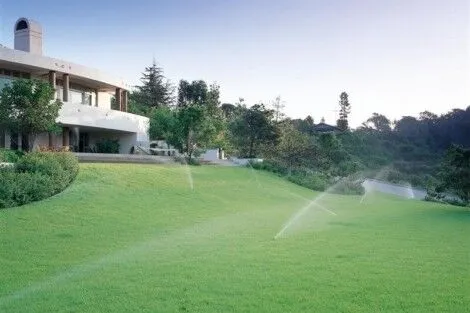 Lush green lawn with sprinklers watering the landscape and outdoor furnishings in Long Island. Beautiful landscaped yard with sprinklers and outdoor furnishings in Long Island.