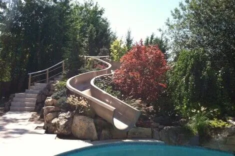 A sleek water slide installed by All Island Group, enhancing outdoor pool area with natural surroundings. Long Island outdoor water slide with lush landscaping and pool.
