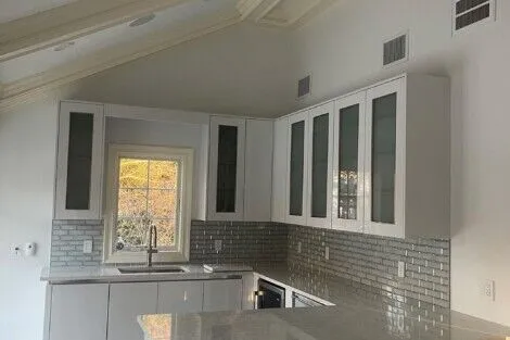 Spacious modern kitchen featuring white cabinets, gray backsplash, and a kitchen island with seating. Contemporary kitchen with white cabinetry and gray backsplash.