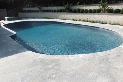 Custom inground pool with stone surround and lush landscaping in Long Island, perfect for outdoor living and relaxation. Beautiful inground pool with stone deck and landscaped yard in Long Island.