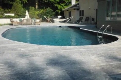 Beautiful inground pool with stone deck, outdoor furniture, and lush greenery in Long Island setting. Inground pool with stone deck and outdoor furniture in Long Island.