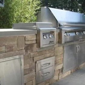 Stainless steel outdoor grill and storage with stone surround.