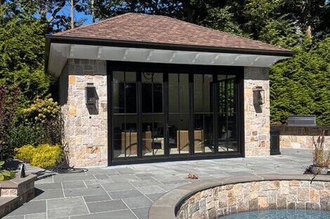 Elegant pool house with stone accents and outdoor furnishings in a lush backyard setting. Modern pool house with stone accents and glass doors in a landscaped backyard.