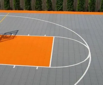A basketball court with orange and gray surface, featuring a hoop and court markings, ideal for outdoor recreation. Basketball court with orange and gray surface and hoop.