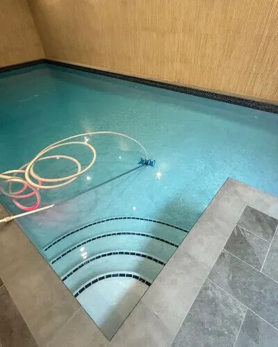 Modern indoor inground pool with steps and cleaning tools, showcasing luxury pool installation services. Indoor inground pool with steps and cleaning equipment in Long Island.