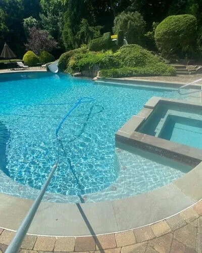 Elegant inground pool with hot tub and lush landscaping in Long Island, perfect for outdoor relaxation. Beautiful inground pool with hot tub and outdoor furnishings in Long Island.