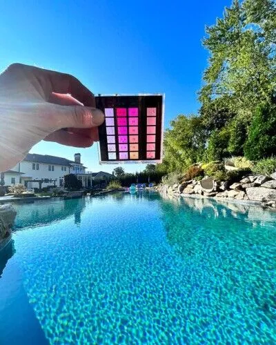 Inground pool with a person holding the pool cover control panel, showcasing outdoor pool installation and maintenance. Person holding pool cover control panel over a clear inground pool on a sunny day.