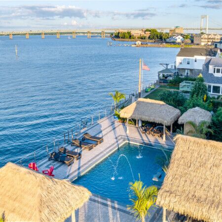 Beautiful Long Island waterfront pool with outdoor seating and thatched roof cabanas.