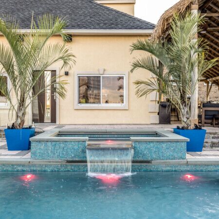 Beautiful inground pool with waterfall, surrounded by palm trees and outdoor seating.