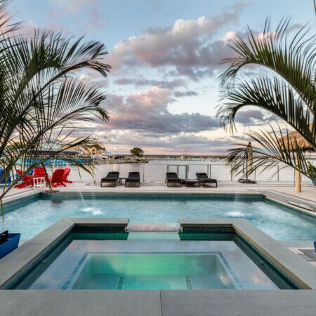 Modern inground pool with hot tub and outdoor furnishings in a scenic setting.