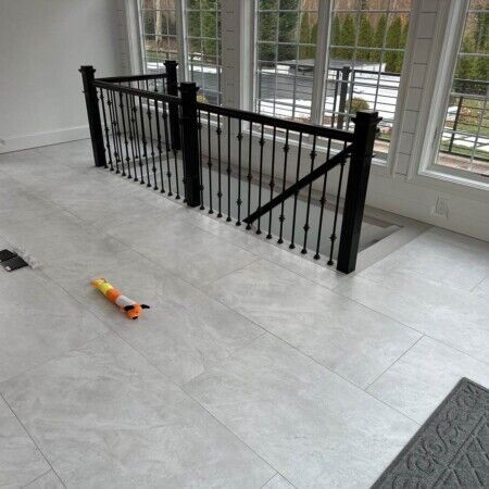 New black metal staircase railing installed in a bright, spacious room with large windows and tiled flooring. Modern black metal staircase railing in bright room with large windows.