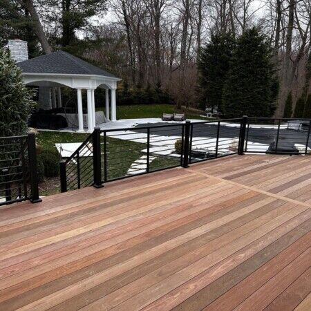 Spacious backyard with a wooden pool deck, gazebo, and outdoor furnishings in Oyster Bay. Beautiful wooden pool deck with black railing and gazebo in backyard.
