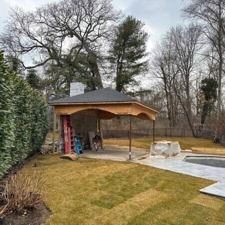 Ongoing inground pool installation with a shaded patio area and surrounding outdoor features in Oyster Bay. Backyard pool construction with a covered patio and outdoor furnishings.
