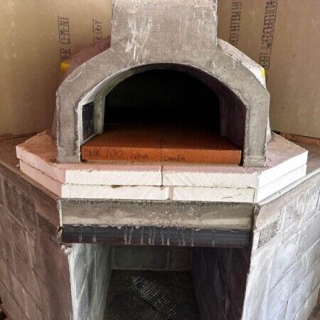Building a custom outdoor pizza oven with concrete and brick for backyard entertainment. Concrete outdoor pizza oven under construction with brick base.