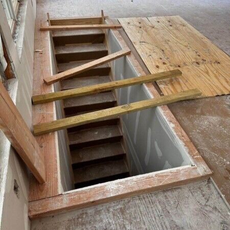 Ongoing inground pool installation with wooden framing and stairs in a residential backyard. Construction of an inground pool with wooden framing and stairs underway.