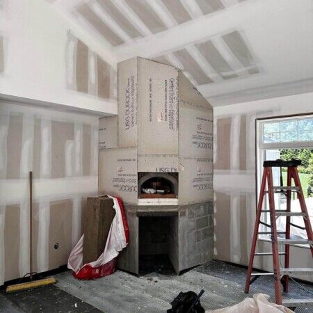 Interior view of a home under construction with an inground pool fireplace and construction tools. Construction of an inground pool with fireplace in a home interior.