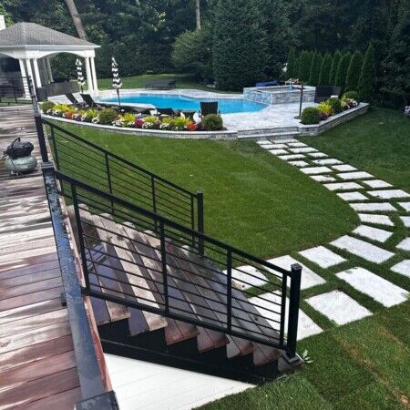 Elegant backyard featuring a swimming pool, stone pathway, and outdoor seating area in Oyster Bay. Beautiful backyard with inground pool, lush landscaping, and outdoor furnishings.