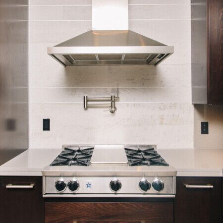 Stainless steel stove with range hood in contemporary kitchen setting.
