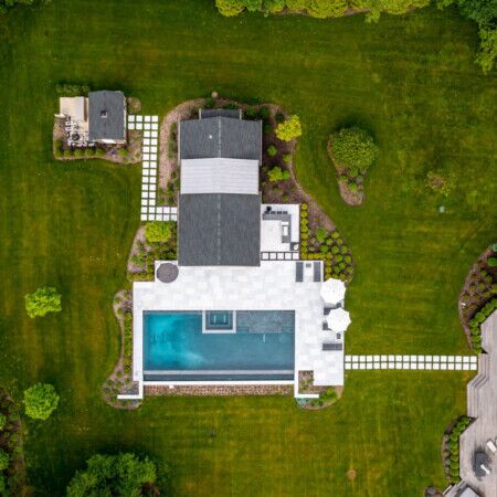 Beautiful backyard with a modern inground pool, outdoor furnishings, and lush landscaping in Syosset, Long Island. Aerial view of a backyard with a pool, patio, and landscaped yard in Syosset, Long Island.