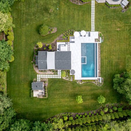 Beautiful backyard with a custom in-ground pool and outdoor living space in Syosset, Long Island. Aerial view of a backyard with a large in-ground pool and outdoor furnishings.