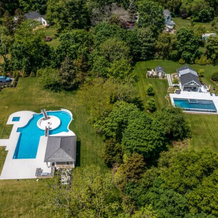 Elegant Long Island backyard featuring an inground pool, outdoor seating, and lush landscaping. Aerial view of a luxurious Long Island backyard with inground pool and outdoor furnishings.
