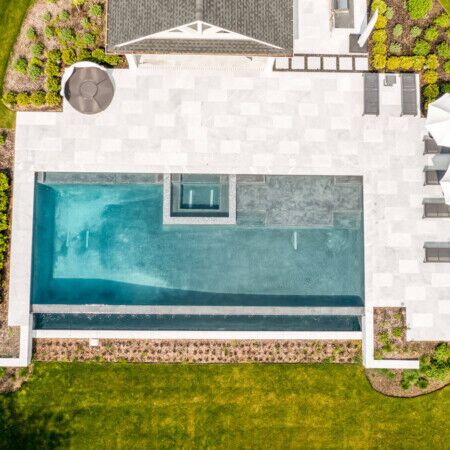 Elegant inground pool with spacious patio, outdoor furniture, and lush landscaping in Long Island. Aerial view of a modern inground pool with surrounding patio and outdoor furnishings.