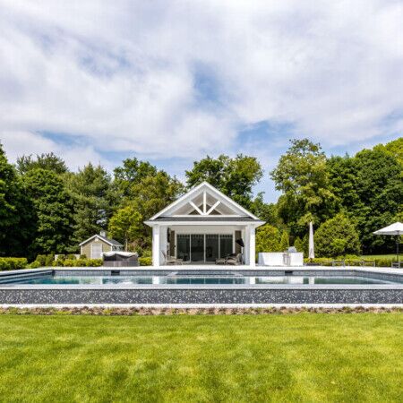 Beautiful inground pool with outdoor pavilion and seating area in a landscaped backyard. Elegant inground pool with outdoor pavilion and lush greenery in Long Island.