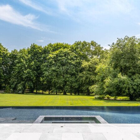 Elegant inground pool with surrounding outdoor furnishings and scenic greenery in Long Island. Luxury inground pool with lush green landscape and clear blue sky.