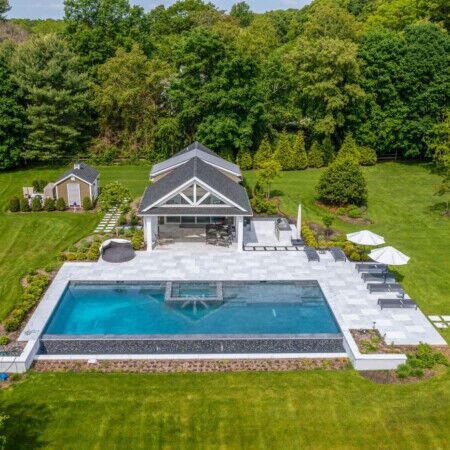 Elegant inground pool with outdoor seating and lush landscaping in a spacious backyard. Beautiful inground pool with outdoor furnishings in a lush backyard.