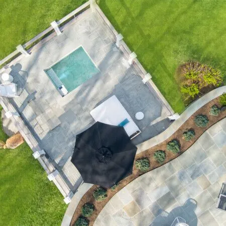 Aerial view of a luxurious backyard with pool, patio, and outdoor furnishings in Long Island.