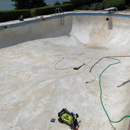 An empty inground pool being renovated, with cleaning tools and hoses present. Empty inground pool during renovation with tools and hoses.