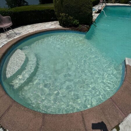 Elegant inground pool with attached spa, surrounded by outdoor furniture and lush landscaping in Long Island. Beautiful inground pool with spa and outdoor furnishings in Long Island.