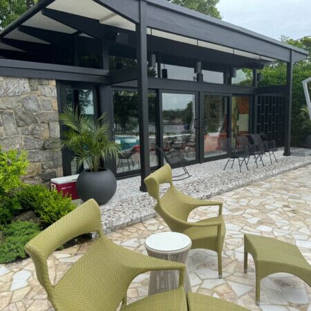 Contemporary outdoor lounge with poolside furniture and glass enclosure at All Island Group, Long Island. Modern outdoor seating area with poolside furniture and glass enclosure.