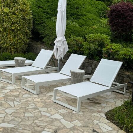 Relaxing outdoor pool lounge area with white chairs, umbrella, and vibrant greenery. Poolside lounge chairs with umbrella and lush garden backdrop.