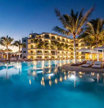Elegant resort pool area with palm trees, lounge chairs, and ambient lighting at dusk. Luxury resort pool with palm trees and outdoor seating at sunset.