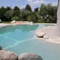 Beautiful inground pool with outdoor furnishings and lush greenery in Long Island. Inground pool with surrounding outdoor furnishings and lush landscape.