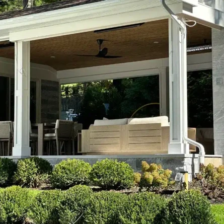 Elegant outdoor living area with seating, ceiling fan, and lush landscaping in Roslyn, Long Island. Covered outdoor patio with seating and ceiling fan in Roslyn.