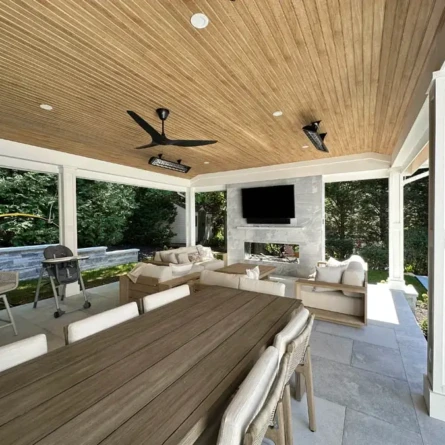Elegant outdoor living area with a covered roof, comfortable seating, and a wall-mounted TV, perfect for relaxing or entertaining. Covered outdoor patio with seating and TV, surrounded by greenery.