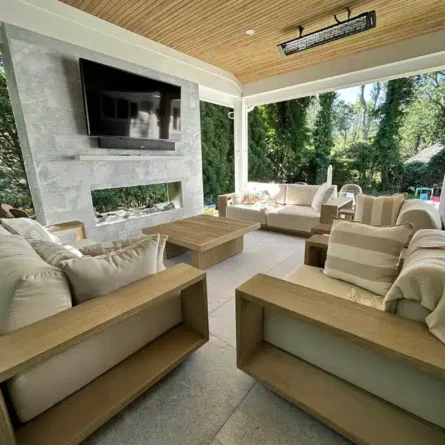 Elegant outdoor living space with cozy seating, TV, and scenic views, perfect for relaxing or entertaining. Outdoor living area with comfortable seating and TV under a roof.