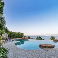 Elegant inground pool with scenic water view, surrounded by lush greenery and outdoor furniture. Luxury inground pool with scenic water view and outdoor furnishings.