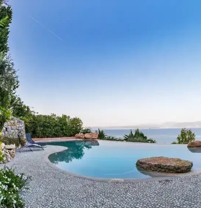 Luxury inground pool with scenic water view and outdoor furnishings.