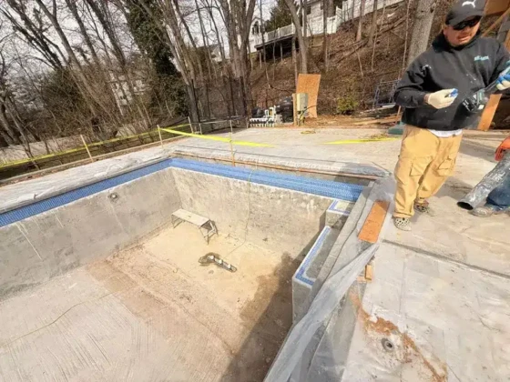 Inground pool construction site with worker inspecting the area.
