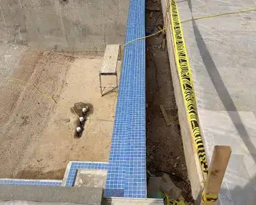 Inground pool installation in progress with blue tiles and safety barriers.
